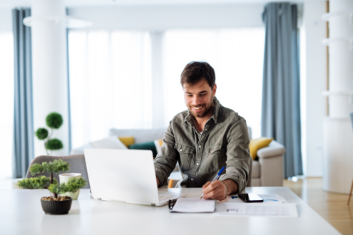 alt="Zufriedener Teilnehmer lernt online am Laptop – flexible Kfz-Gutachter Ausbildung bequem von zu Hause aus" Mann mit Laptop und Notizen in einem modernen, hellen Wohnraum.