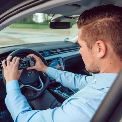 alt="Kfz-Sachverständiger fotografiert Fahrzeugschaden vom Fahrzeuginneren – mobile Beweissicherung im Gutachtenprozess" Mann sitzt im Auto und bedient ein Navigationsgerät am Steuer.